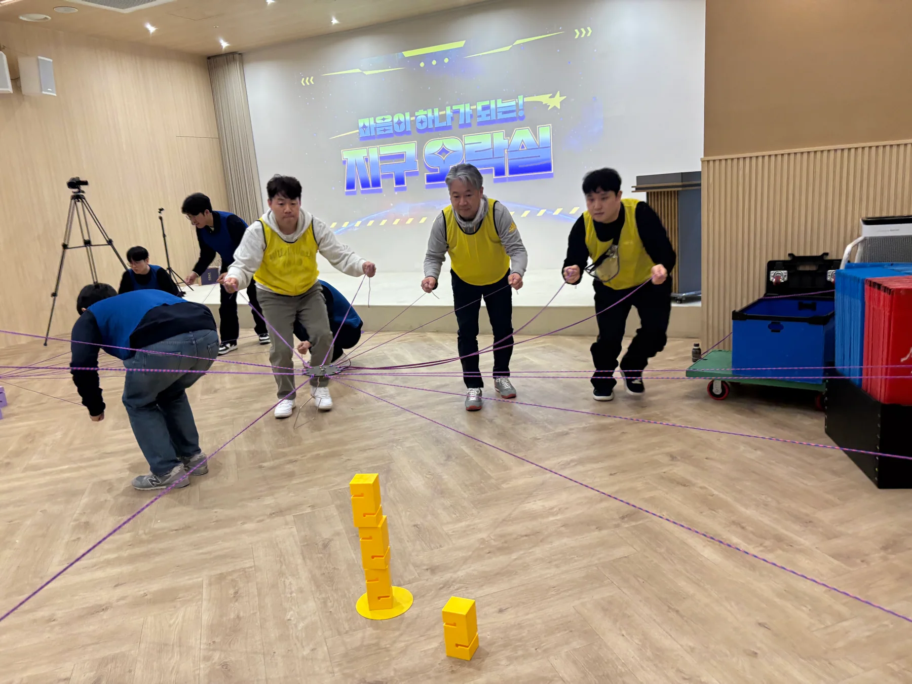 노란 팀 참가자들이 여러 줄을 함께 조작해 블록 탑을 쌓는 실제 팀빌딩 현장